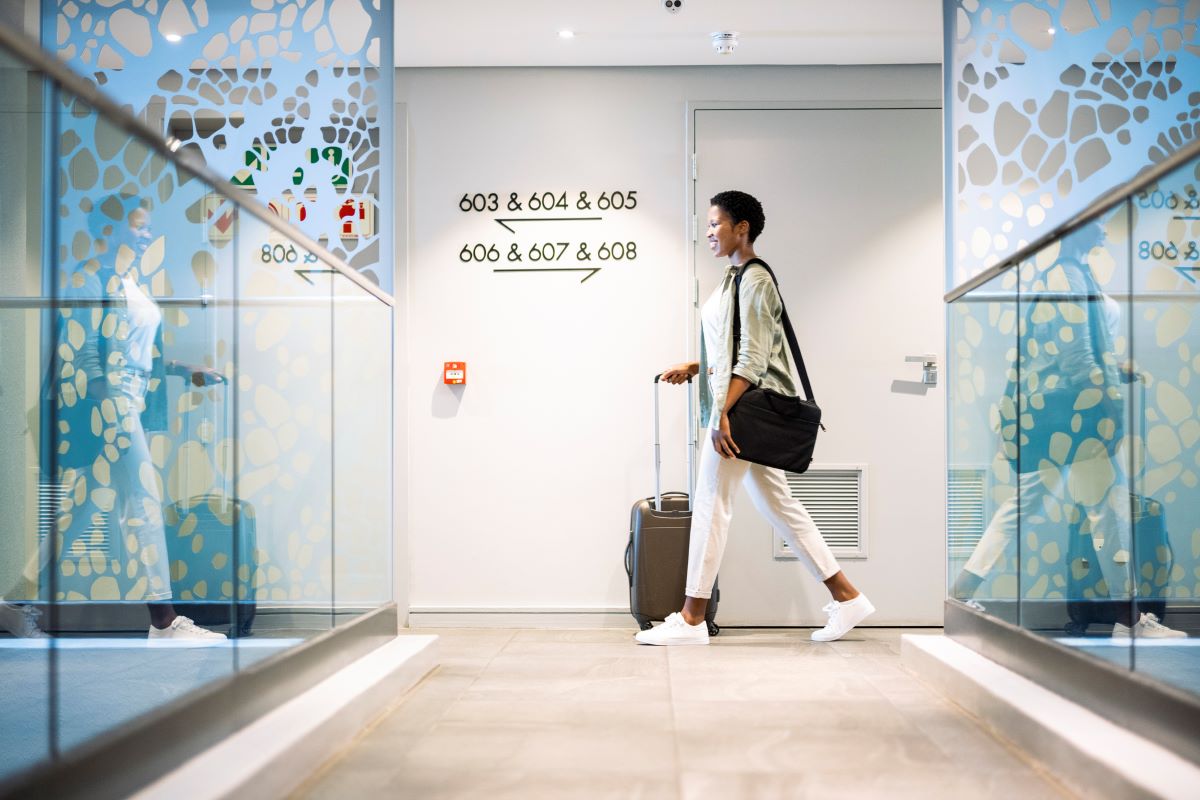 Woman walks across corridor in hotel carrying luggage