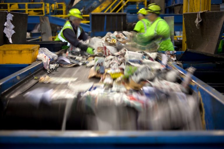 Workers separating paper and plastic on a conveyor belt in a recycling facility